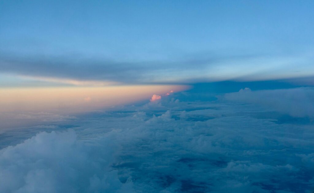 View from an airplane window showing a sunset horizon with clouds below, fading from orange to blue.