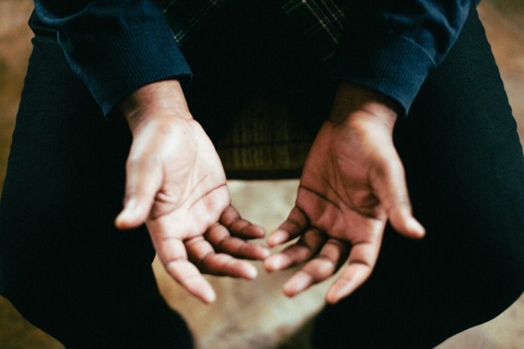 Close-up of a person sitting with open hands resting on their lap, palms facing up.