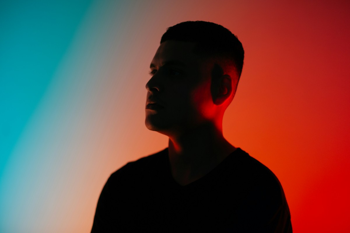 Silhouette of a person with short hair against a vibrant gradient background of blue and red tones.