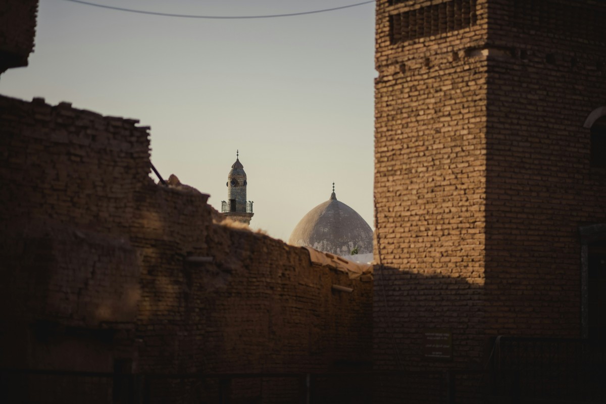 A distant mosque dome and minaret partially visible between old brick buildings under a clear sky.
