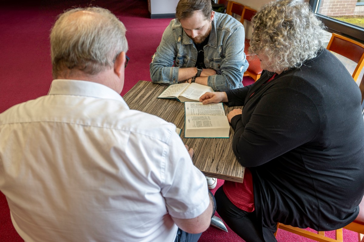 Three people sitting around a table, reading and discussing documents in a room with a red carpet.