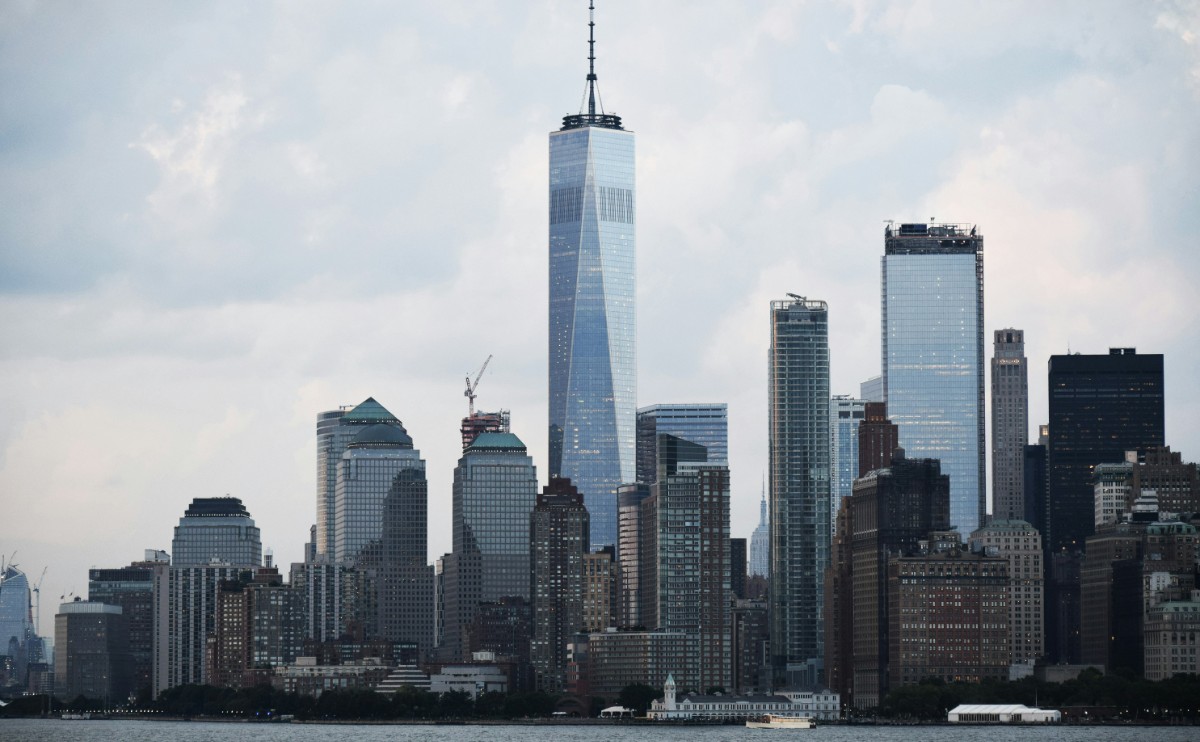 Skyline of New York City featuring tall skyscrapers, including the One World Trade Center, under a cloudy sky.