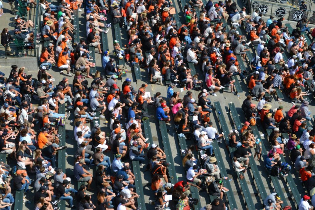 Crowd sitting in rows of stadium bleachers, many wearing orange and black clothing.