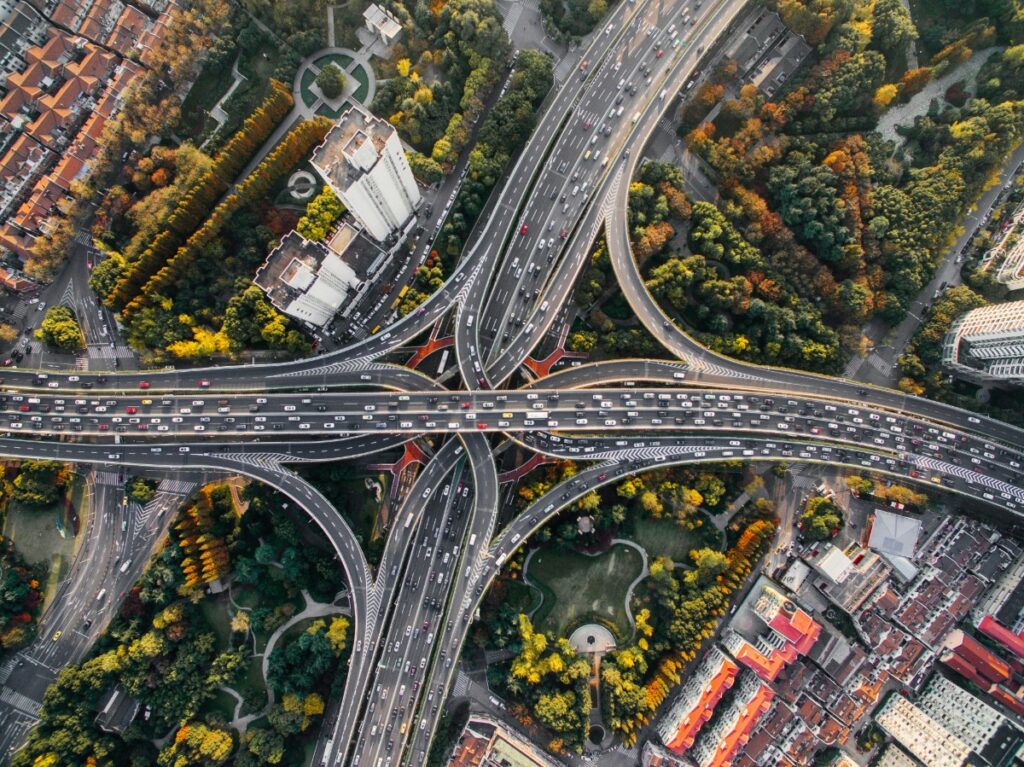Aerial view of a busy highway interchange surrounded by buildings and trees, showing multiple intersecting roads and overpasses.