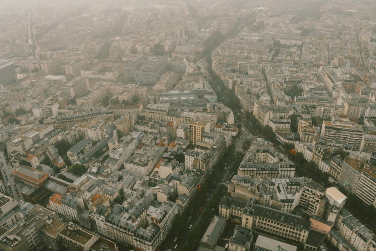 Aerial view of a dense urban landscape with numerous buildings, streets, and a prominent avenue running through the cityscape under a cloudy sky.