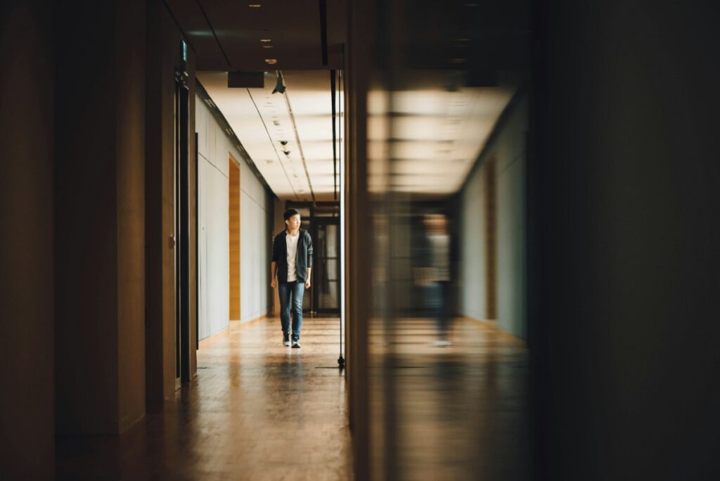 Person walking down a dimly lit corridor with reflections on a glass wall.