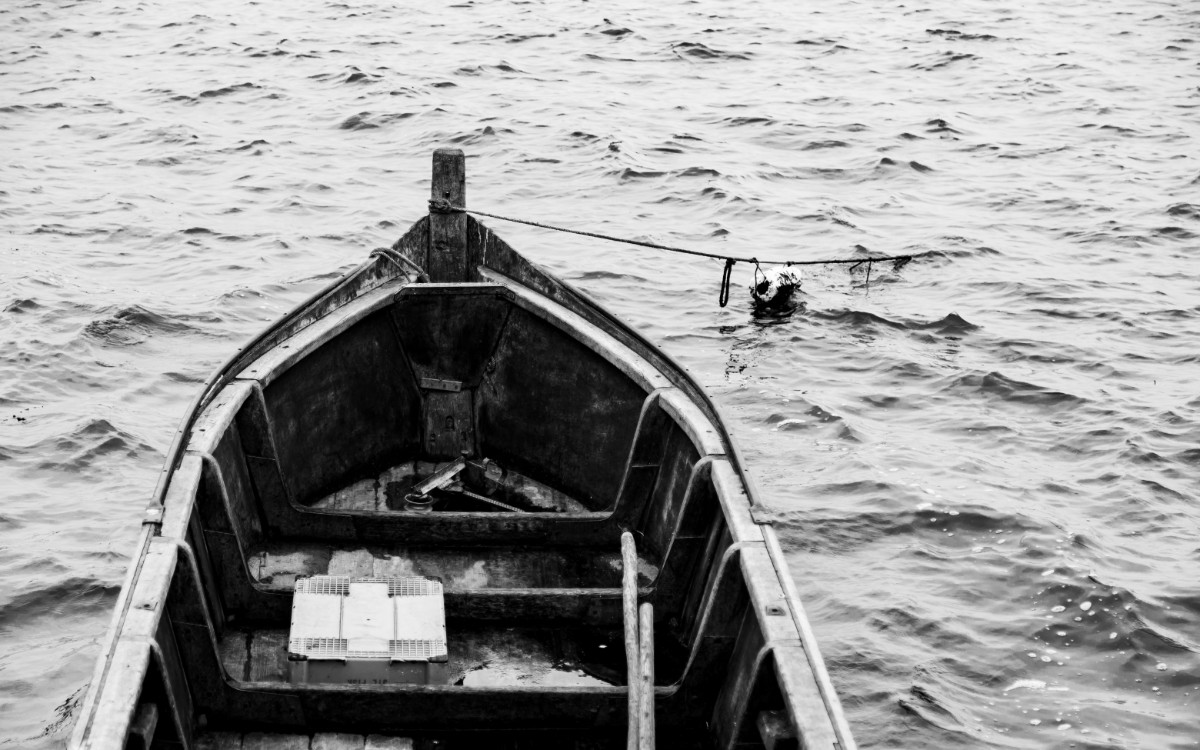 A rowboat with packages inside floats on a choppy body of water, captured in black and white.