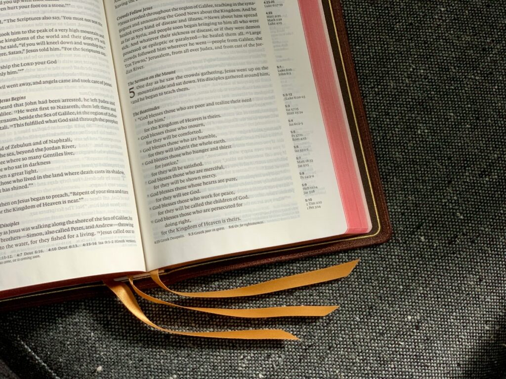 Open book with visible text and three orange ribbons as bookmarks, placed on a dark textured surface.