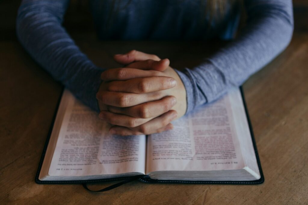 Hands clasped over an open book on a wooden table.