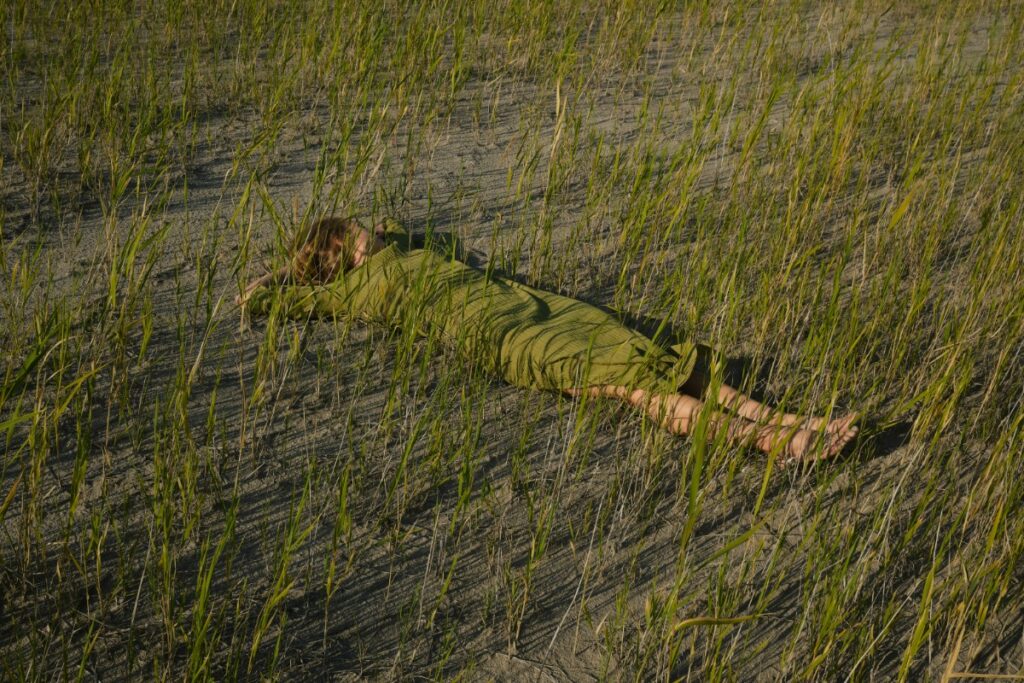 Person in a green outfit lying on the ground among tall grass.