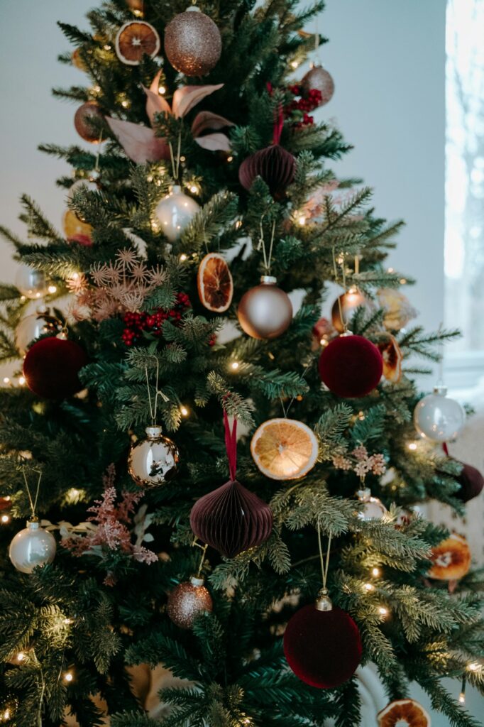Decorated Christmas tree with various ornaments and lights in a room with a large window.