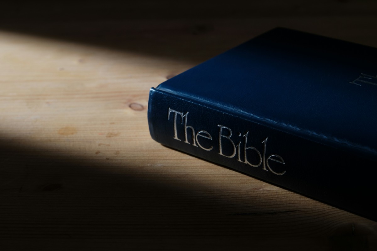 A blue hardcover Bible lies on a wooden surface, partially illuminated by soft light.