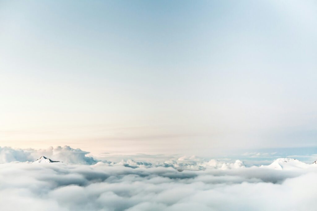 View of a cloudy sky from above, with soft white clouds and a pale blue horizon.