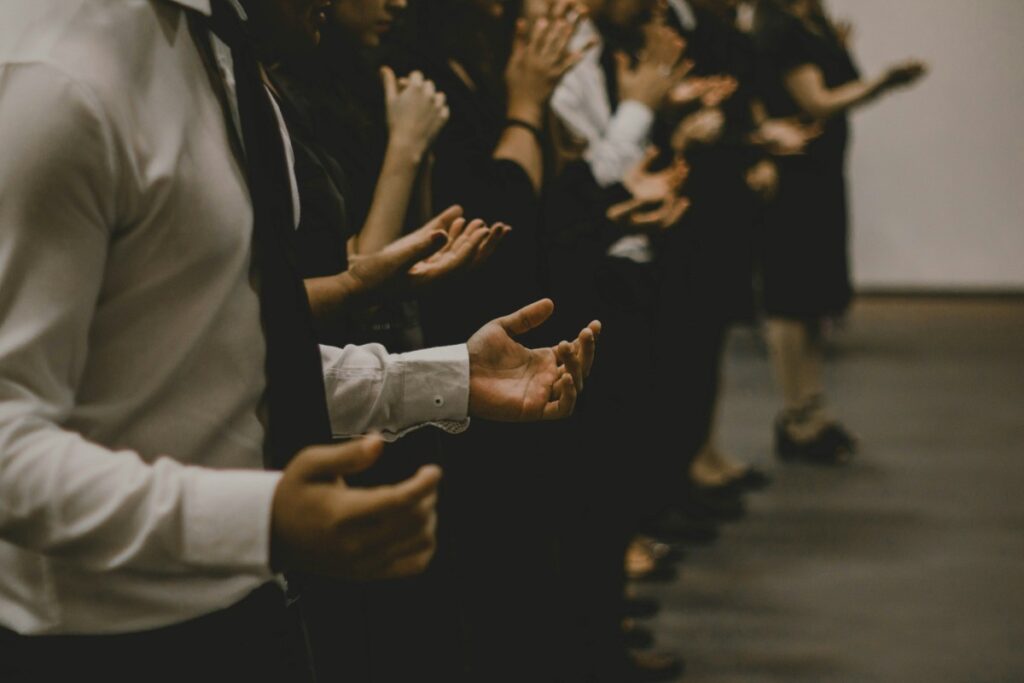 A row of people standing with their hands raised in a gesture, wearing formal attire.