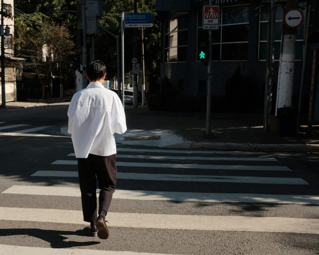 Person in a white shirt crossing a street at a crosswalk, approaching a green pedestrian signal.