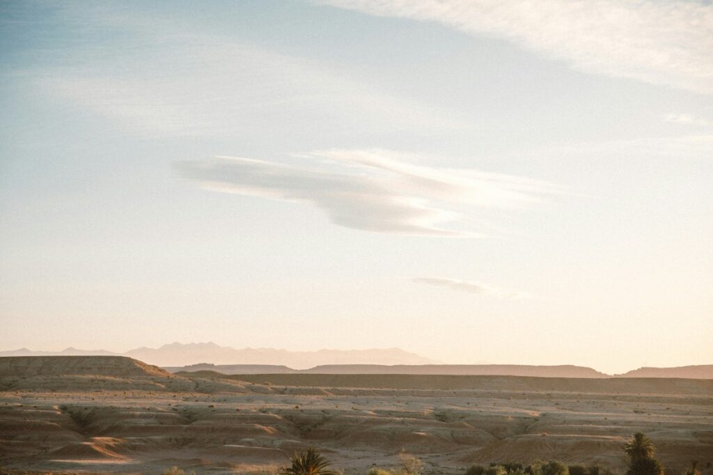 A vast desert landscape with distant hills under a blue sky and scattered clouds.