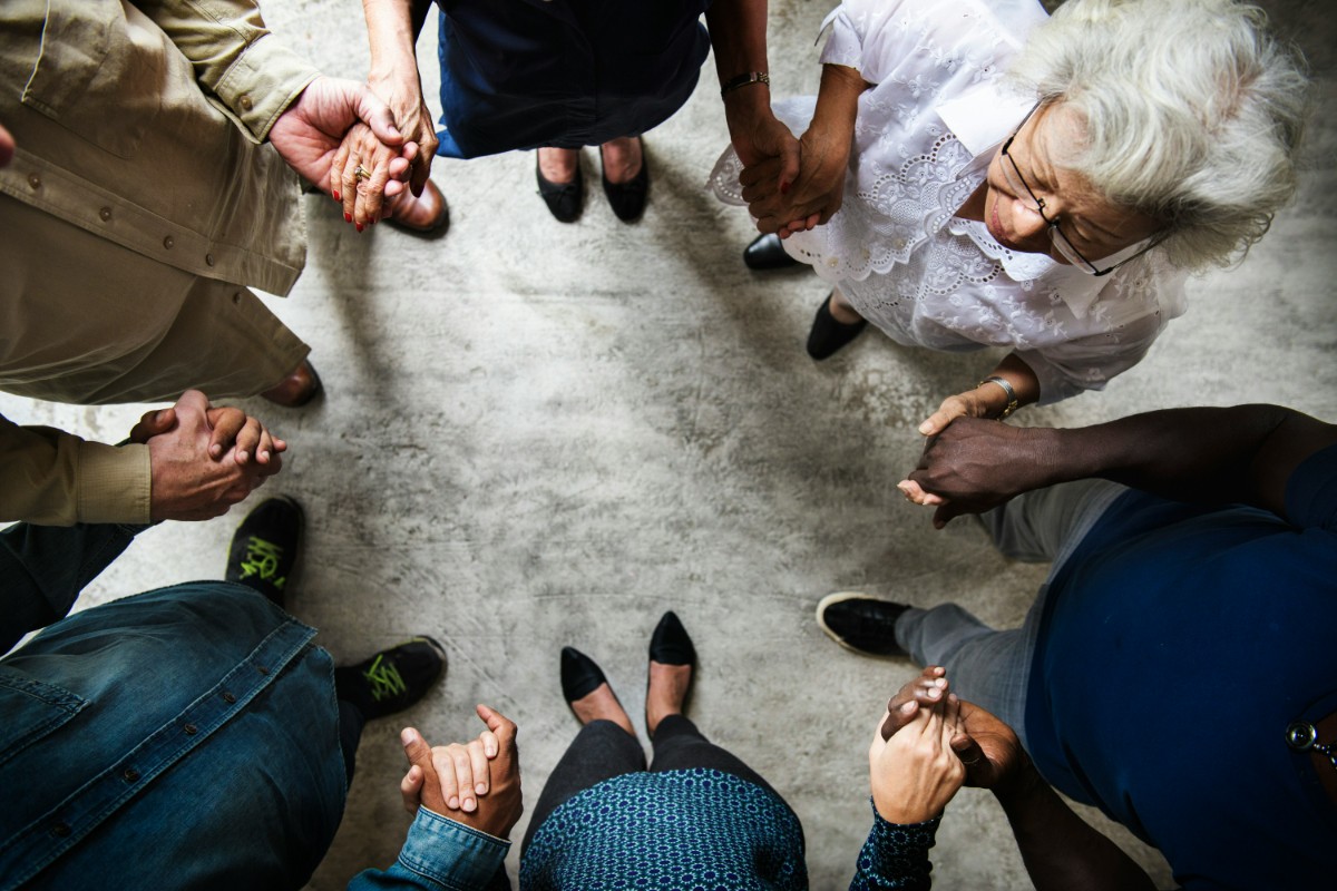 A diverse group of people standing in a circle, holding hands and facing each other.