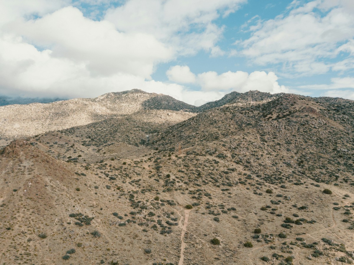 Aerial view of a hilly landscape with sparse vegetation under a partly cloudy sky.