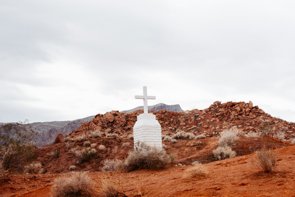White cross on a rocky desert hill under a cloudy sky.
