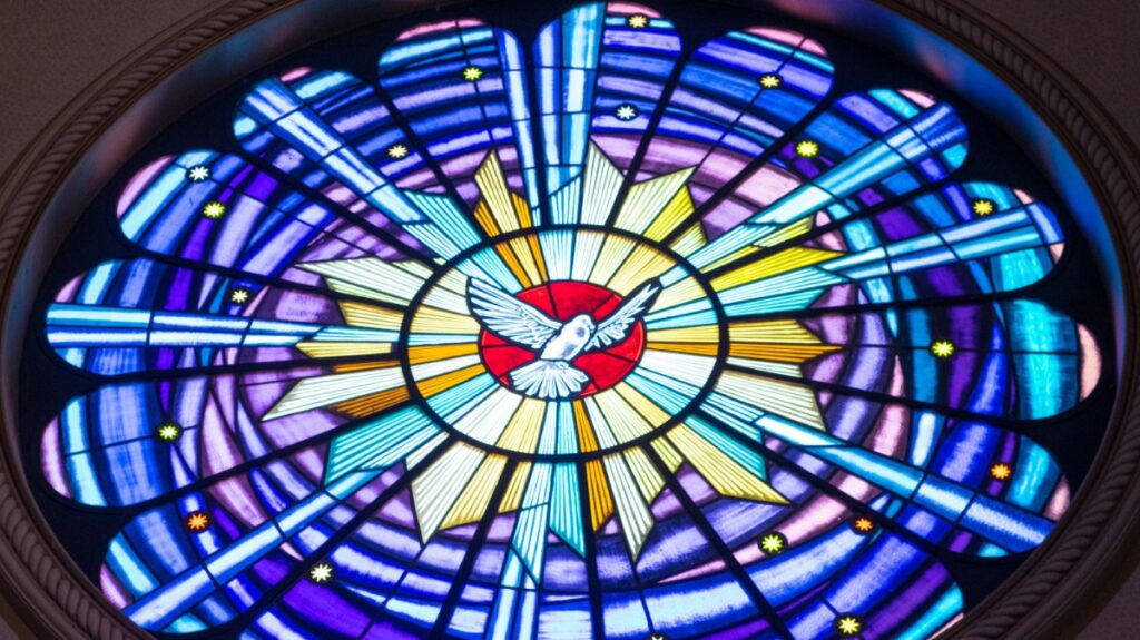 A circular stained glass window depicting a white dove in the center, surrounded by vibrant rays of blue, purple, and yellow.