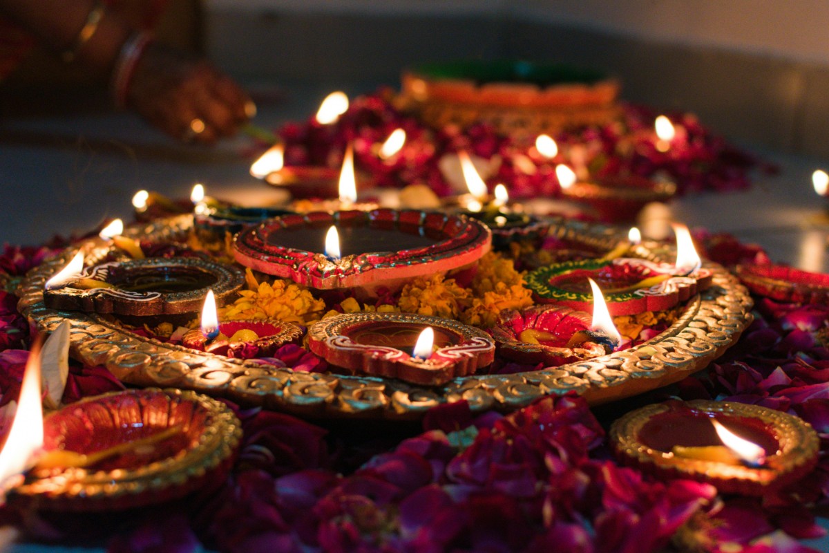 Lit oil lamps surrounded by flower petals, arranged on a decorative plate for a festive setting.