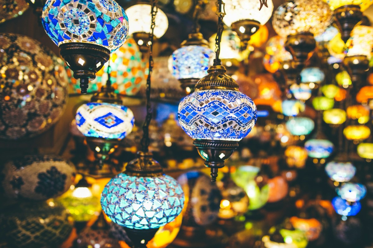A variety of colorful, intricately patterned mosaic lamps are hanging and illuminated in a dimly lit space.