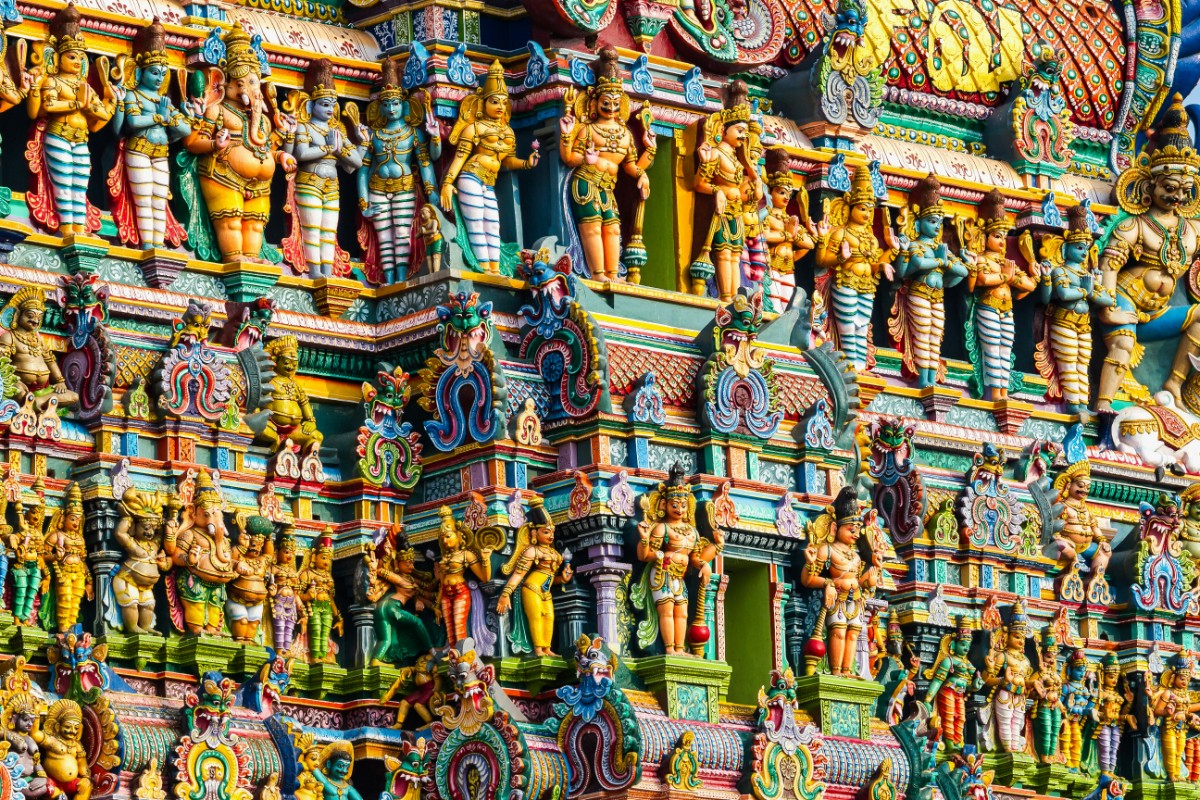 Colorful, intricate carvings and statues adorn the facade of a Hindu temple, featuring numerous deities and ornamental details.