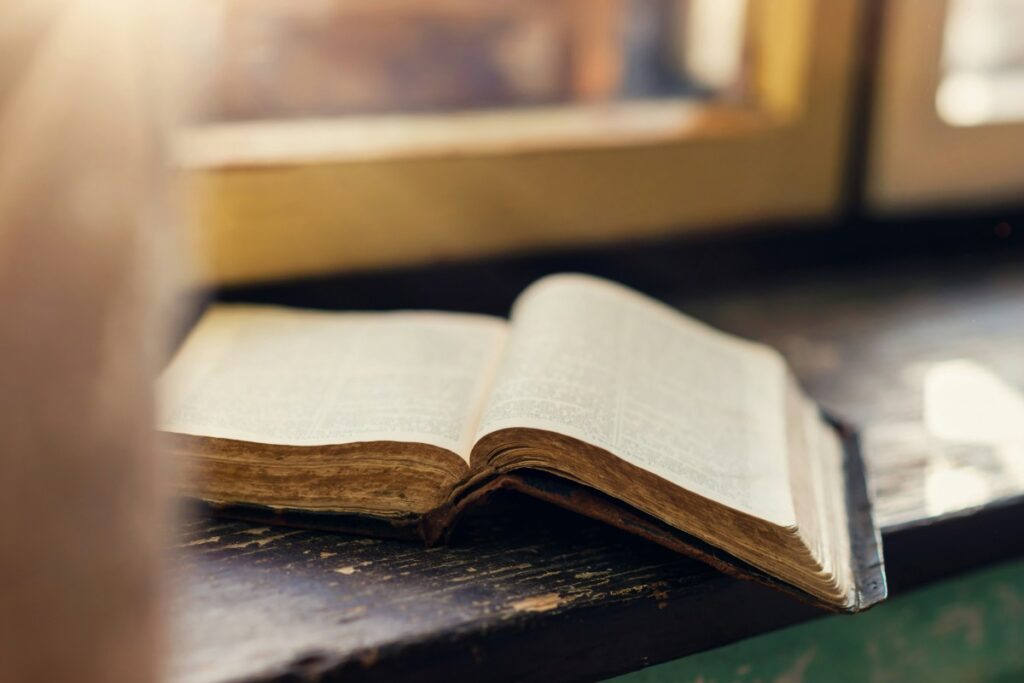 An open book with yellowed pages lies on a wooden windowsill, illuminated by soft natural light.