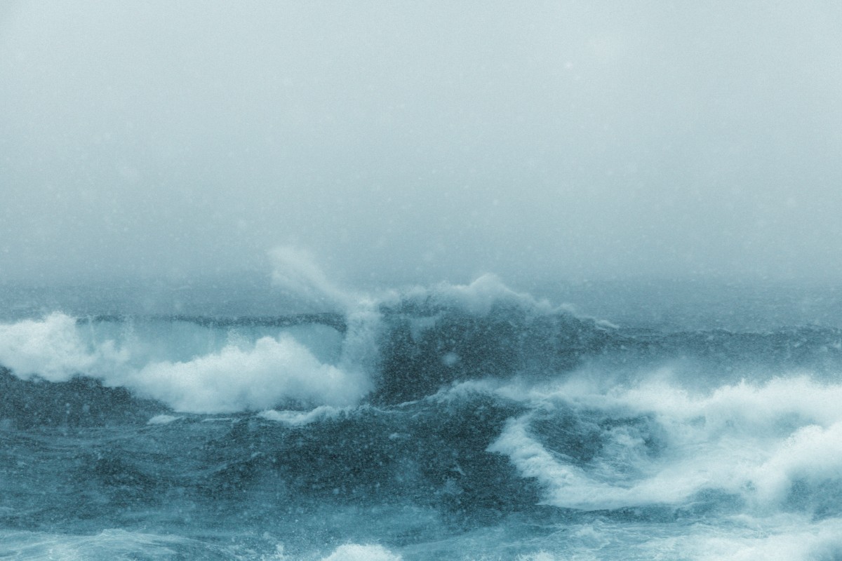 Rough ocean waves under an overcast sky, with visible whitecaps and swirling water.