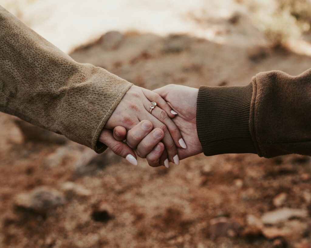 Two people holding hands outdoors, wearing long-sleeved clothing, against a blurred natural background.