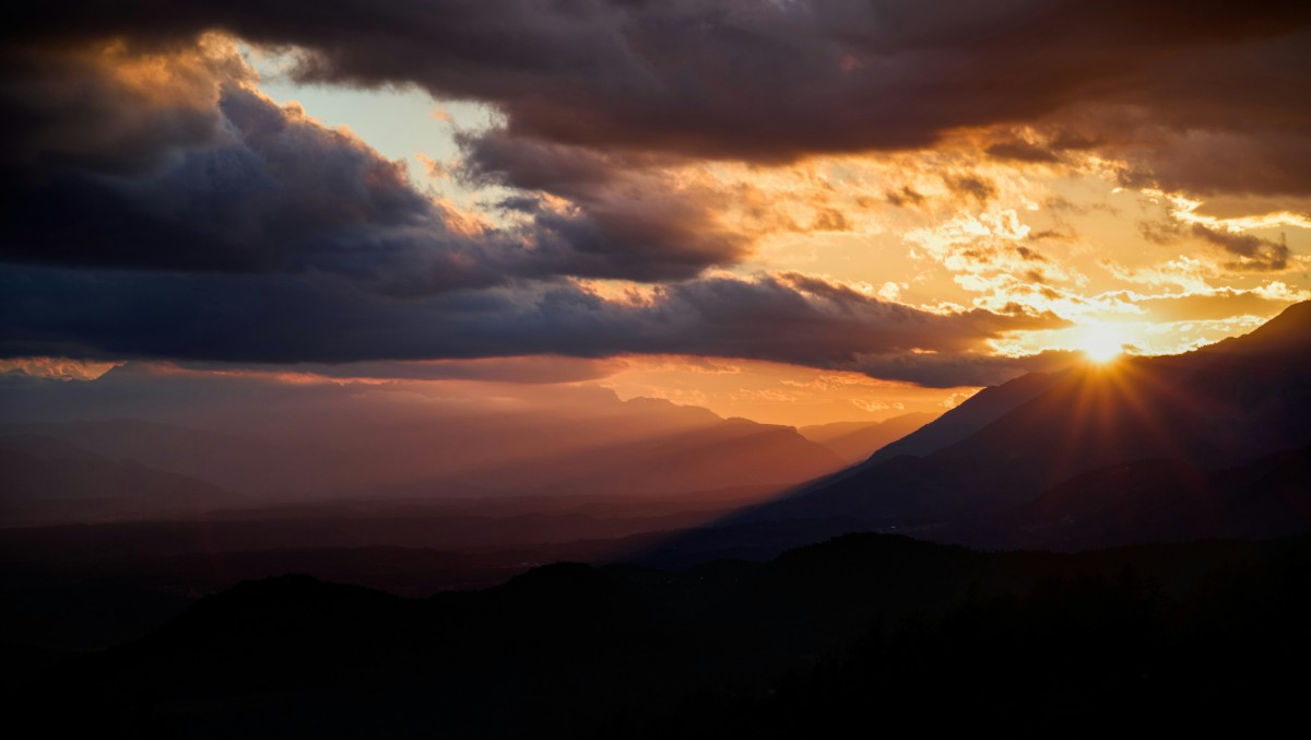 Sunset over a mountain range with dramatic clouds and rays of sunlight breaking through.