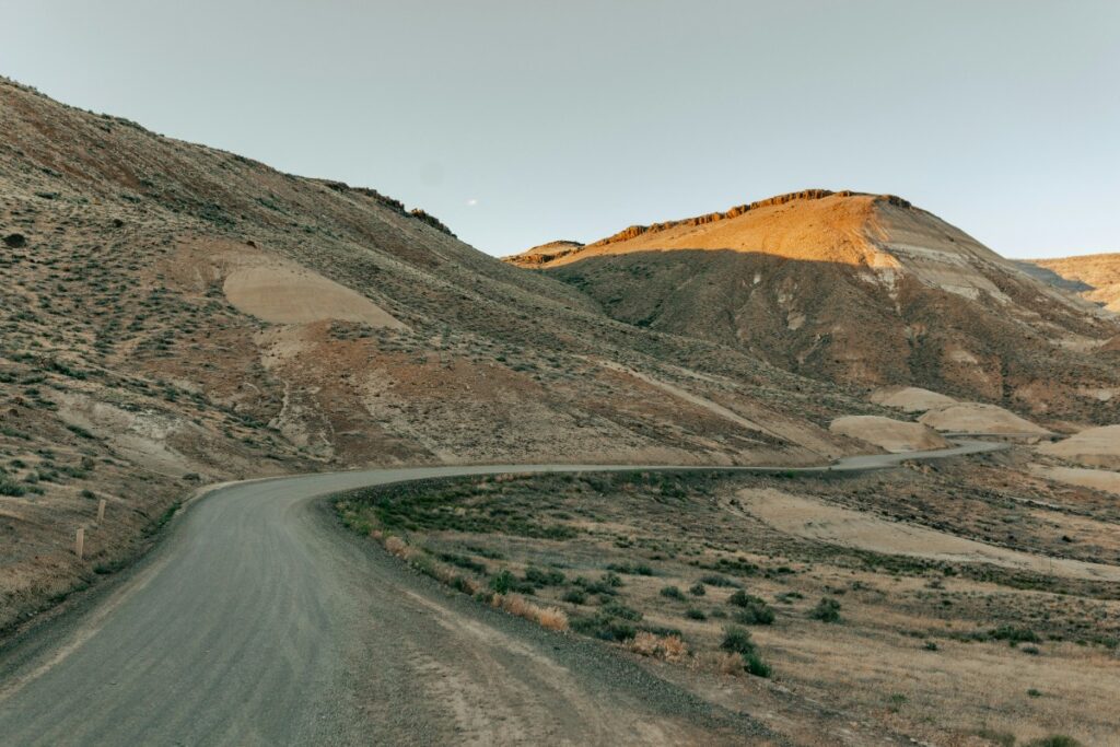 A winding, narrow road curves through a barren, hilly landscape under a clear sky.