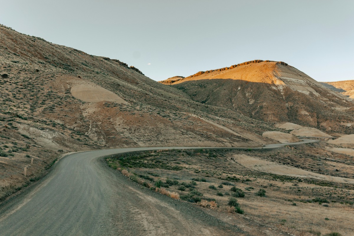 A winding, narrow road curves through a barren, hilly landscape under a clear sky.