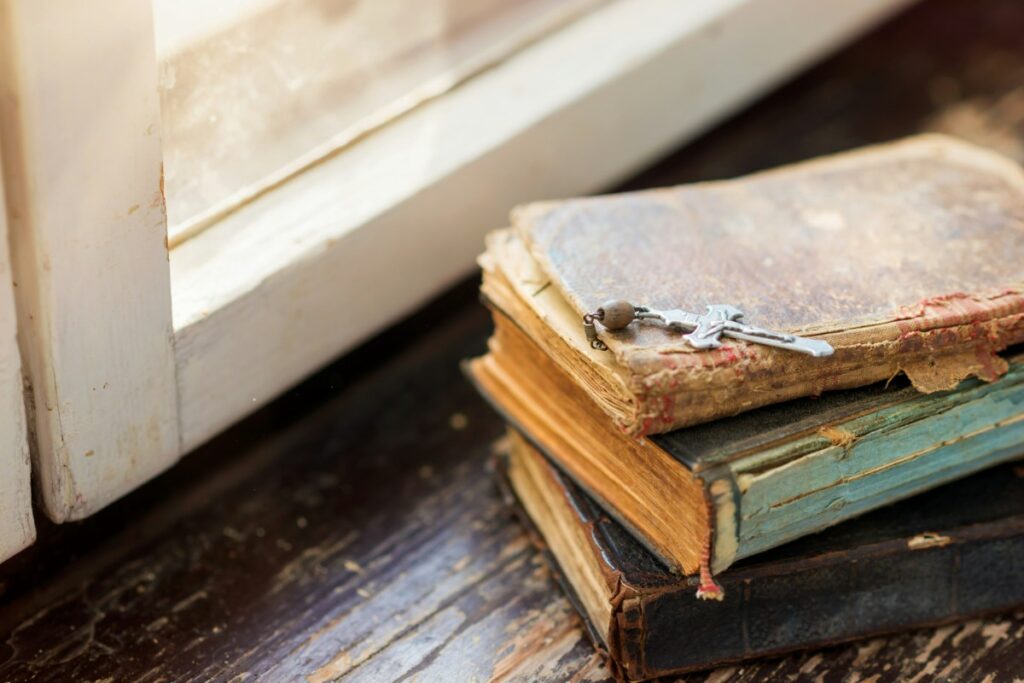 Three worn books stacked by a sunlit window, with a small key resting on top.