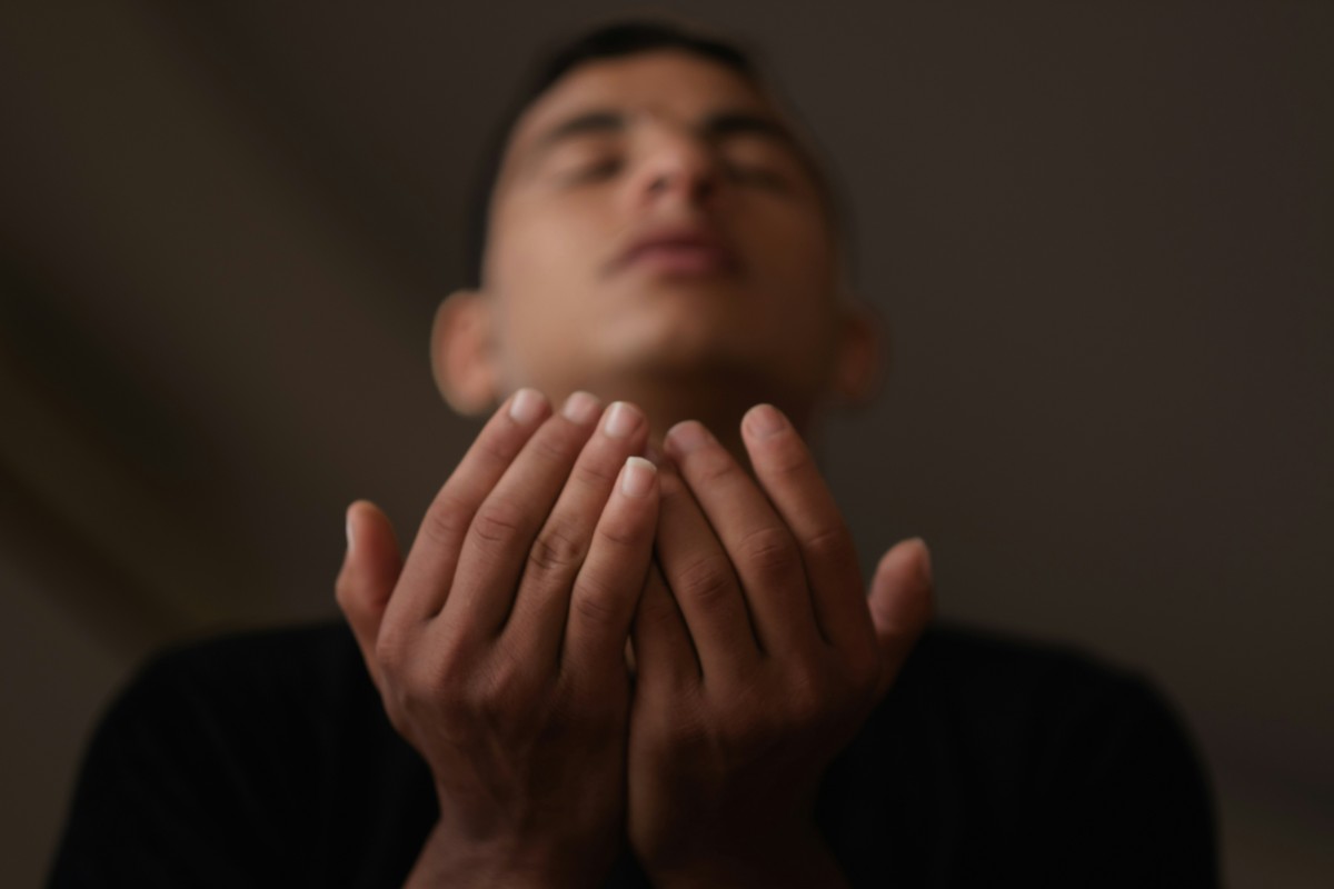 Person with closed eyes holding hands up in a gesture of prayer or contemplation.