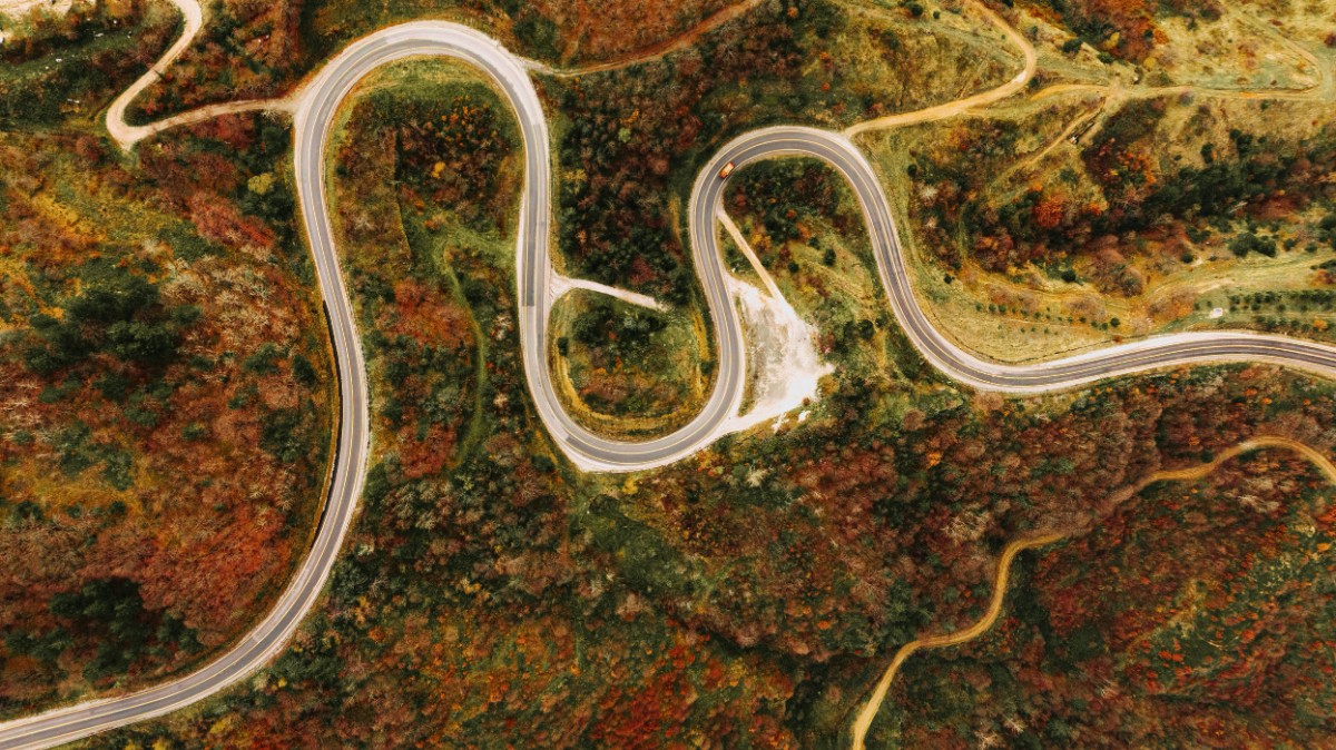 Aerial view of a winding road through a hilly landscape with autumn foliage.