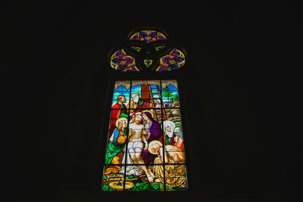 Stained glass window depicting a biblical scene with multiple figures in colorful robes and historical garments.