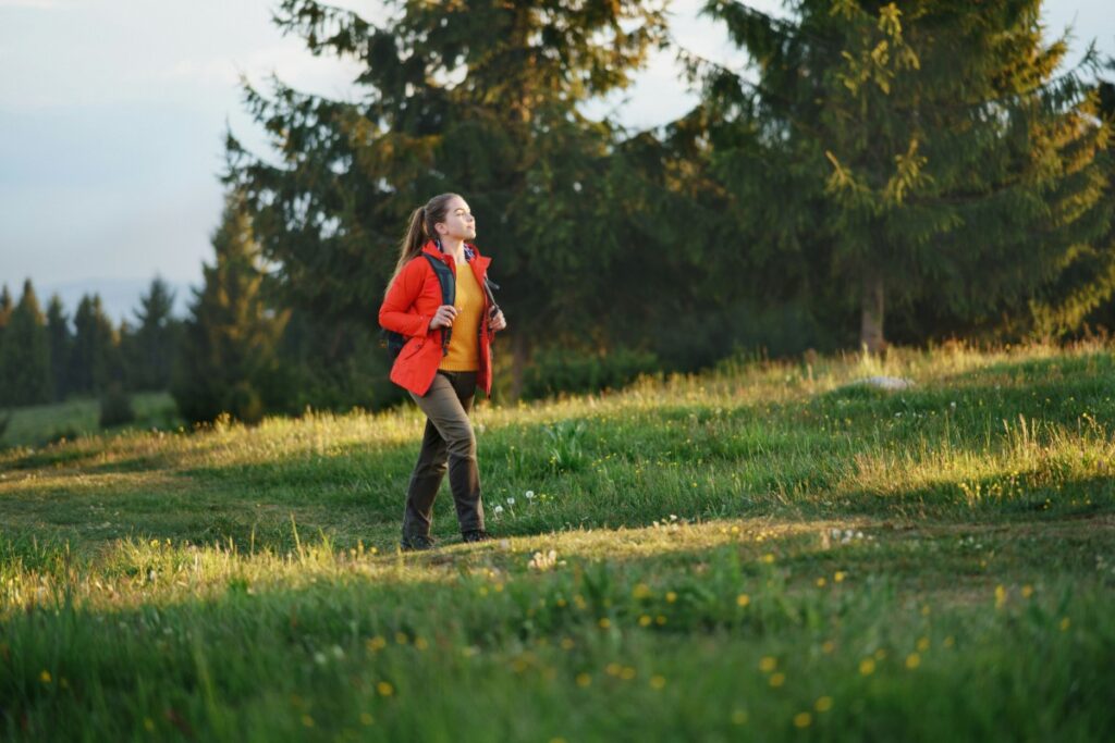 A person in a red jacket jogs on a grassy path surrounded by trees and greenery.