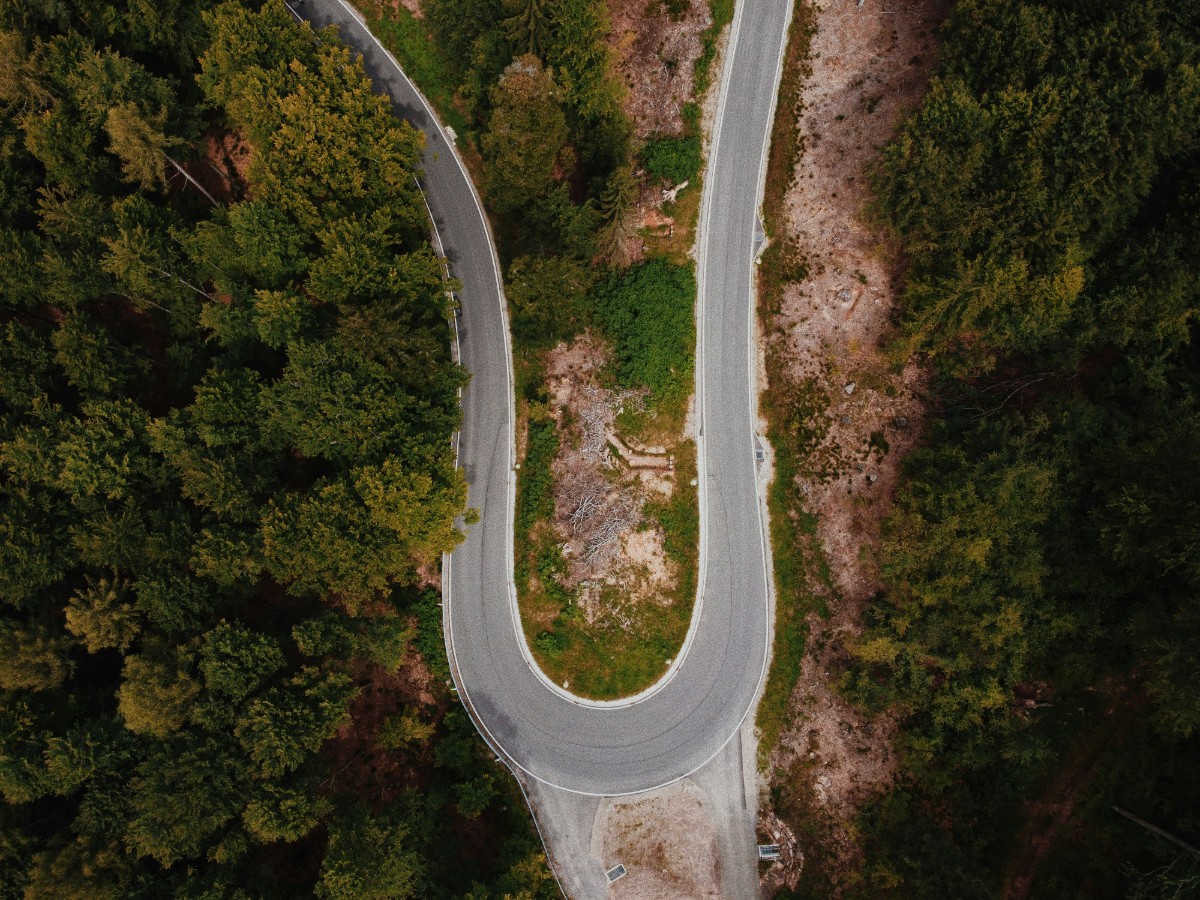 Aerial view of a winding road surrounded by dense green forest, with the road forming a sharp curve.