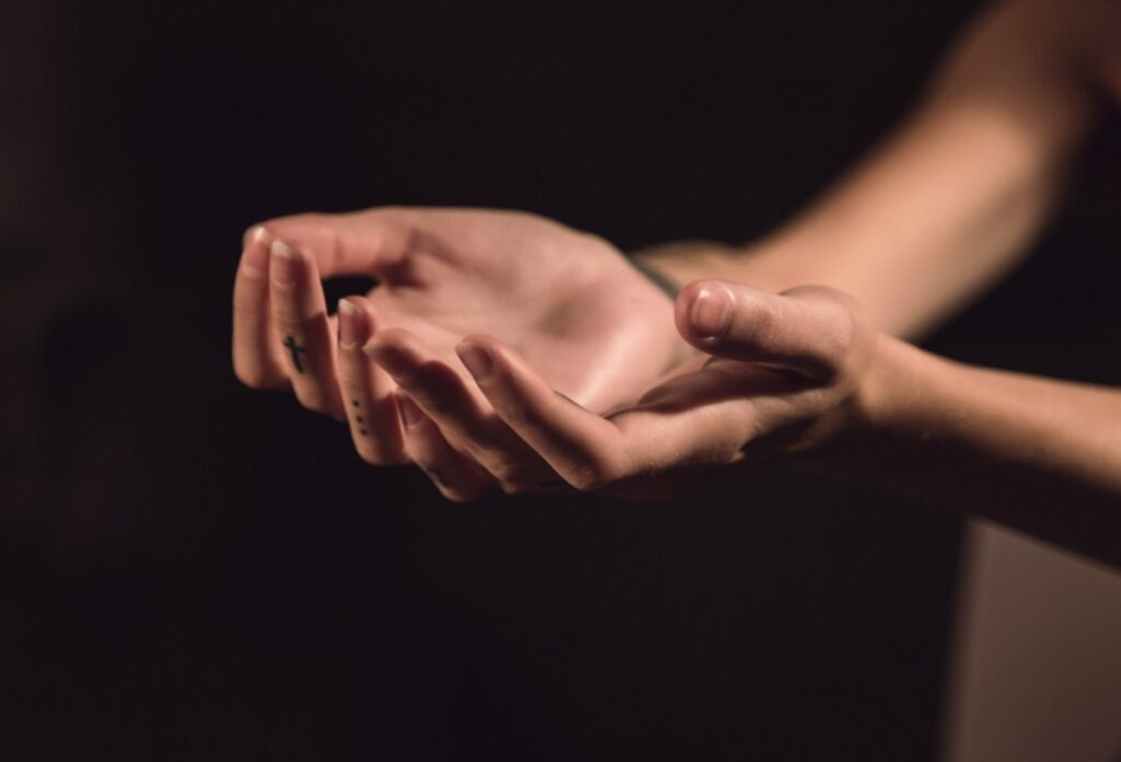 A pair of open hands is extended against a dark background, palms facing upwards.