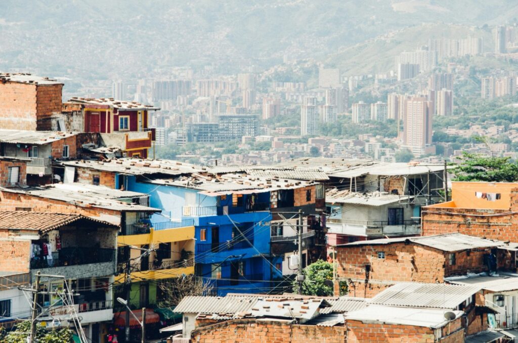 Colorful hillside buildings with mixed materials overlook a distant cityscape under a hazy sky.