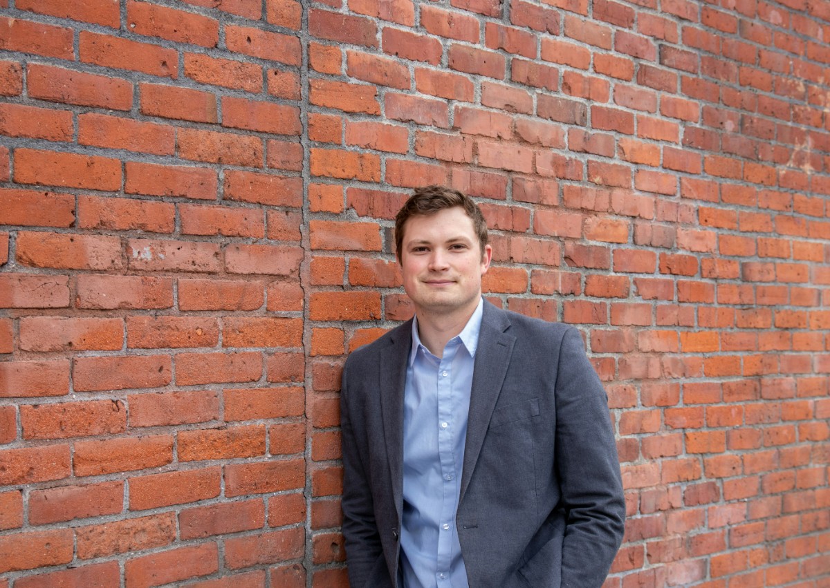 Person in a suit standing against a red brick wall.