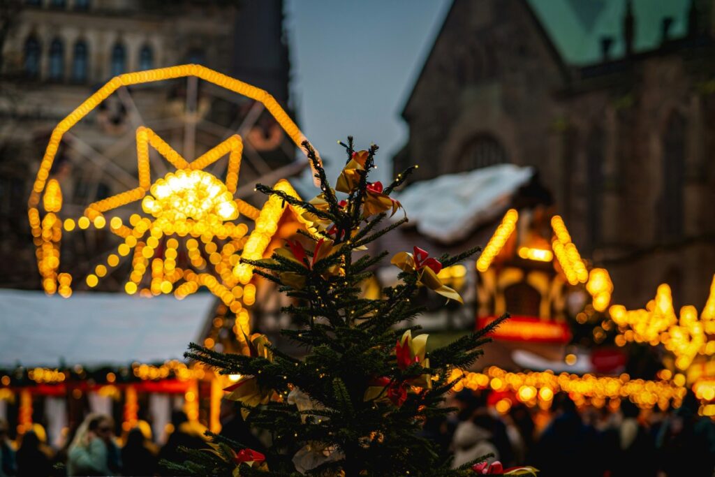 Christmas market at night with a decorated tree and illuminated ferris wheel in the background.