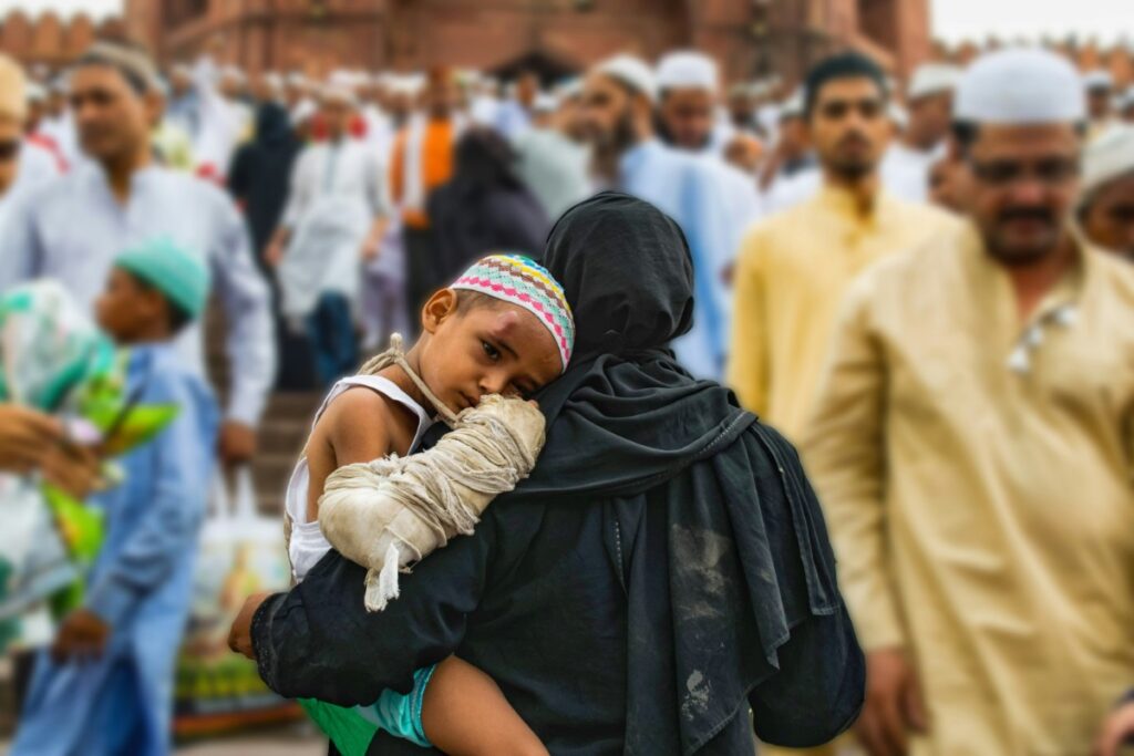A woman in a black garment holds a young child wearing a colorful hat amidst a crowded scene.