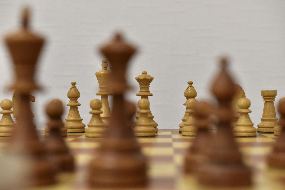 HD photo capturing a close-up of a chessboard with brown and beige pieces. The focus is on the center, where the chess game unfolds with pieces strategically facing each other.