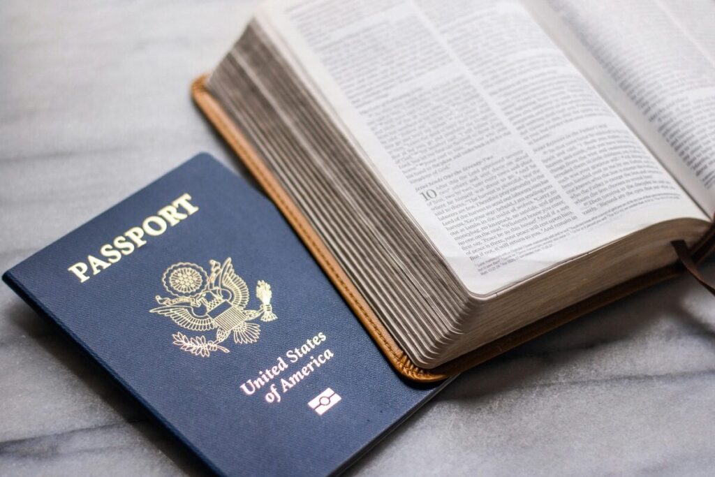 A United States passport and an open book, possibly a Bible, are placed side by side on a gray surface.