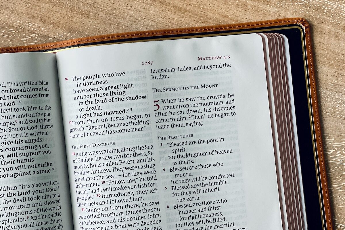 An open Bible lies on a wooden surface, displaying text from the book of Matthew, chapter 4.