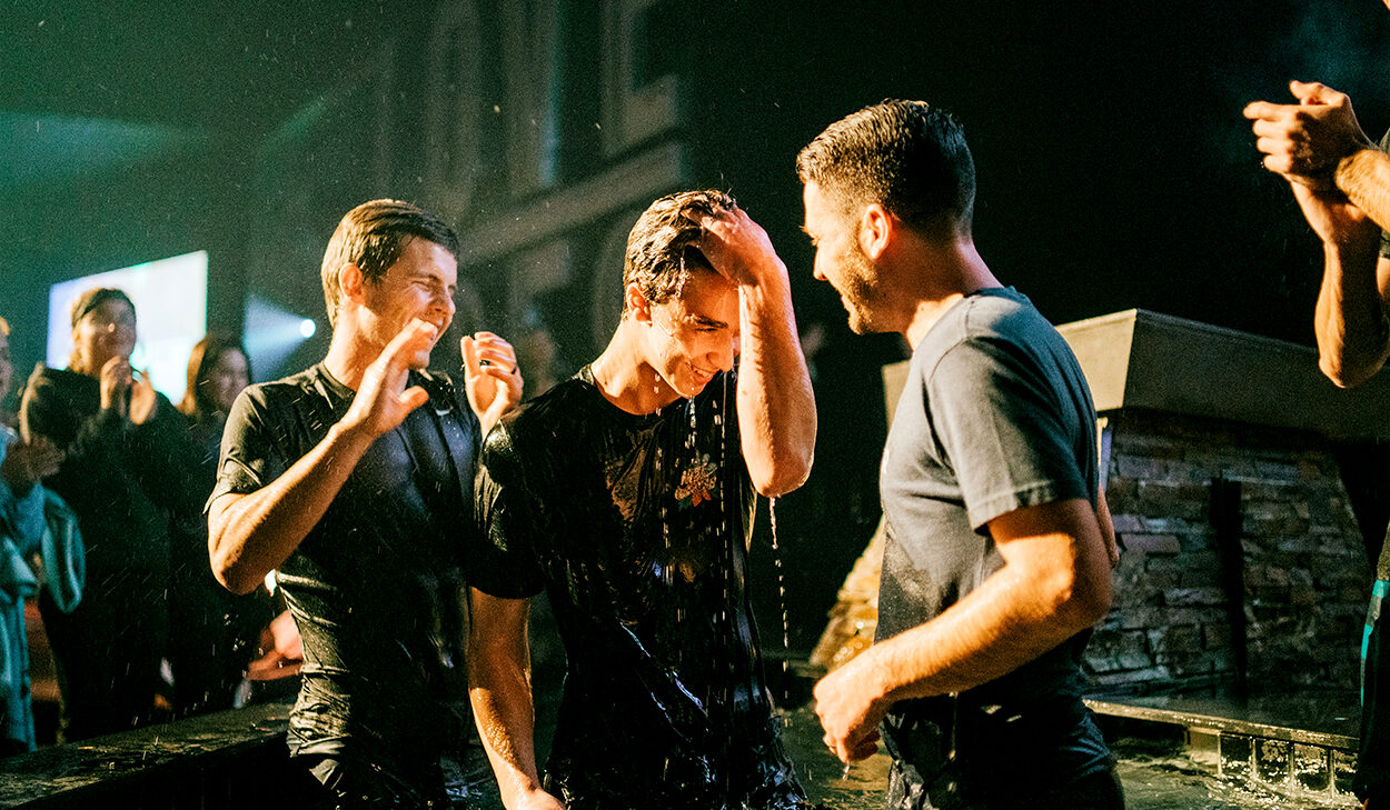 A man at a church stands up after being baptized. He's surrounded by other church members at a service.