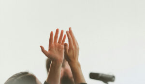 east-west-Arise 28 A woman lifts her hands up in worship. A microphone is seen in the background.