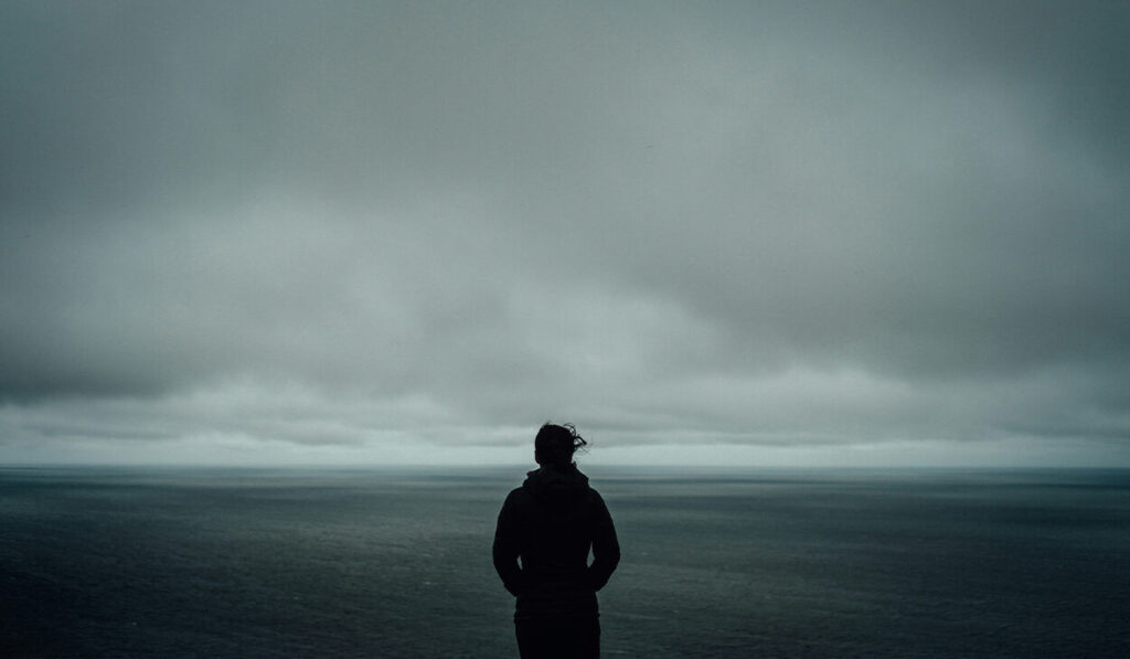A person in a coat stands in front of a foggy field with an overcast sky.